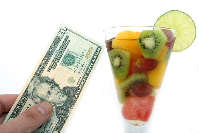 Glass of cut up fruit and hand holding American money r/t health